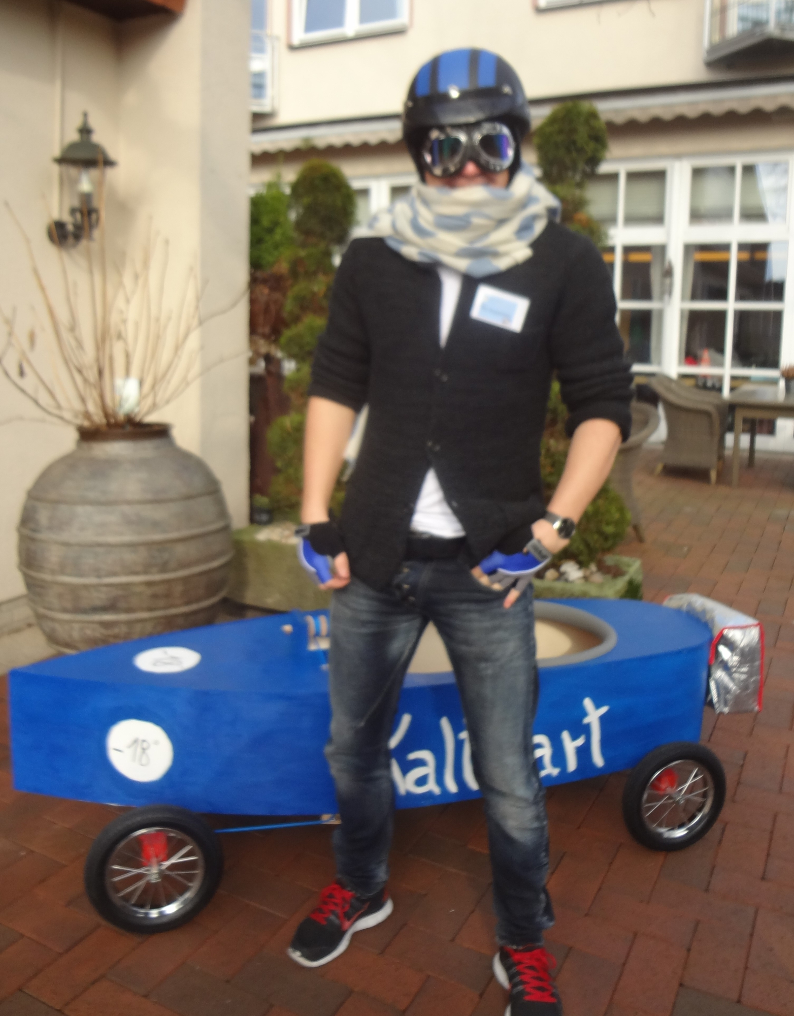 Teilnehmer einer Teamentwicklung mit Helm und Fliegerbrille vor einer selbst gestalteten blauen Seifenkiste